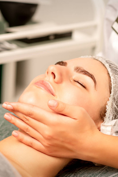 Facial massage. Hands of a masseur massaging neck of a young caucasian woman in a spa salon, the concept of health massage - Fotó, kép