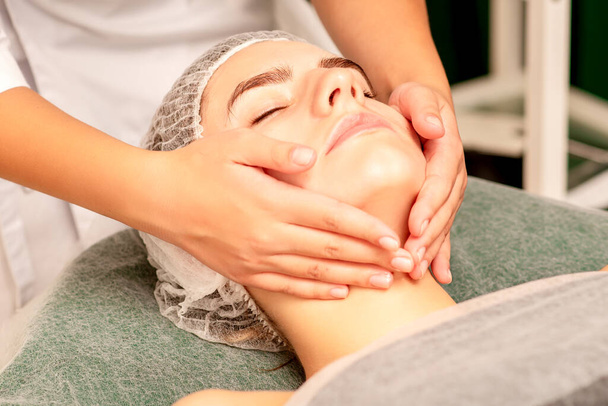 Facial treatment massage. Beautiful young caucasian woman with perfect skin receiving face and neck massage at a beauty spa - Zdjęcie, obraz