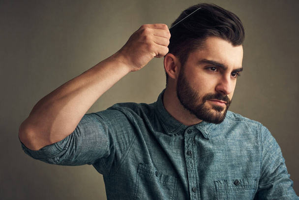Wear that beard proudly. Studio shot of a handsome young man combing his hair against a grey background - Fotografie, Obrázek