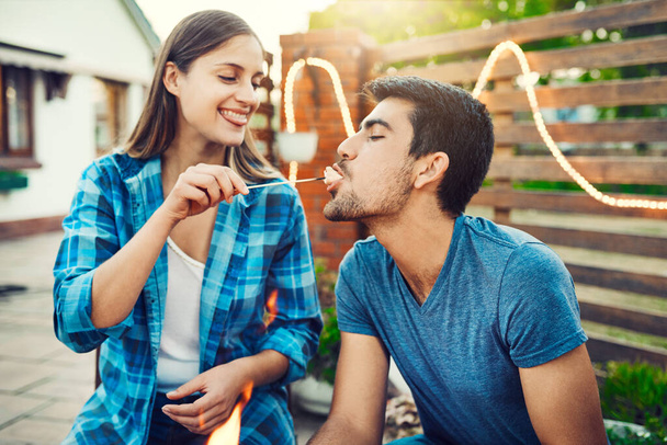 Heres a treat for you. a young cheerful man being fed a marshmallow by his girlfriend while relaxing outside - Photo, image