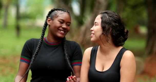 Two diverse friends laughing and smiling together. Mixed race girlfriends talking in conversation outside. Authentic real life laugh and smile - Кадры, видео