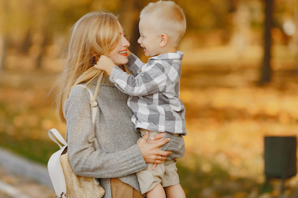 Family in a autumn park. Mother in a brown sweater. Cute little boy in a shirt - Photo, image