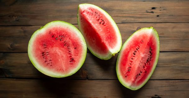 There is a watermelon on a wooden table. half and two quarters of watermelon are on the table. WOODEN-based red, ripe watermelon. - Foto, Imagen