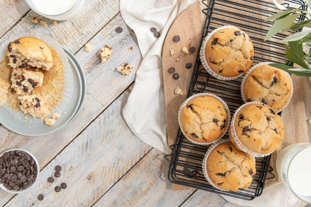 Chocolate chip muffins on a baking rack and glasses of milk on a white kitchen countertop.  Morning breakfast table. Top view, flat lay - Foto, imagen