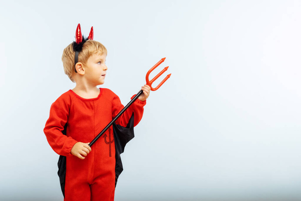 Щасливого Хеллоуїна! Симпатичний маленький хлопчик в костюмі диявола Хелловін з рогами і тризубом на світло-блакитному тлі
. - Фото, зображення
