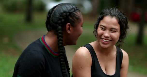Two diverse friends laughing and smiling together. Mixed race girlfriends talking in conversation outside. Authentic real life laugh and smile - Felvétel, videó