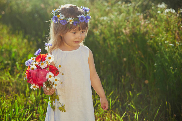 charming child in linen dress walks in a field with flowers at sunset - Photo, image