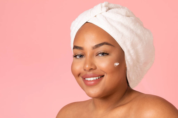 Facial Skincare. Portrait Of Attractive Obese Black Woman Moisturizing Face Posing With Moisturizer Cream Dots On Cheeks Smiling To Camera Over Pink Background In Studio. Beauty Routine Concept - Zdjęcie, obraz