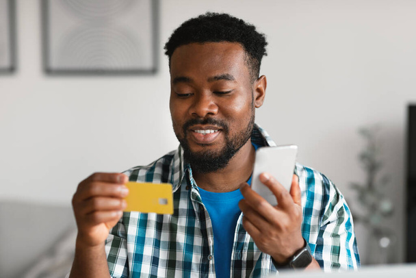 Мобильные покупки. Афроамериканец с помощью кредитных карт и смартфонов делает платежи сидя дома. Банковская заявка и концепция электронной коммерции. Селективный фокус - Фото, изображение