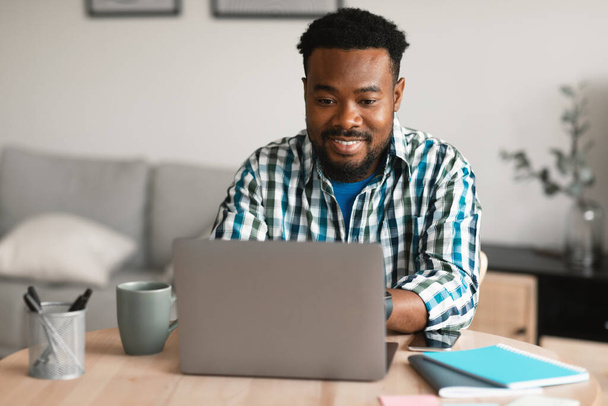 Successful African American Entrepreneur Man Using Laptop Computer Browsing Internet And Working Online Sitting At Home. Professional Freelance Career And Remote Job Concept - 写真・画像