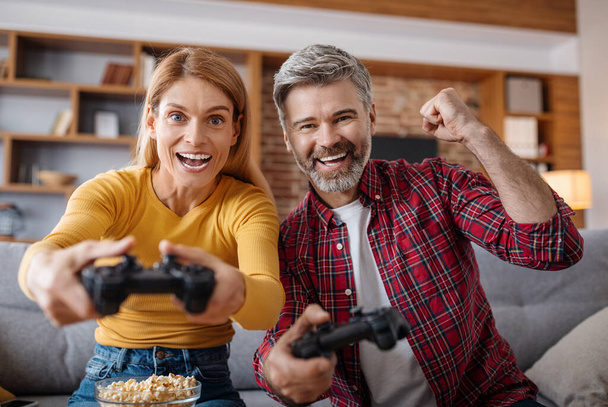 Glad excited adult caucasian female and male with joysticks play in online game in free time, celebrate victory in room interior, close up. Win, fun together at home, entertainment and people emotions - Foto, immagini