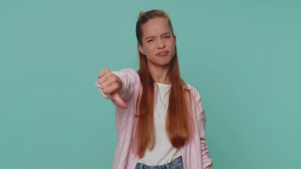 Upset lovely pretty teenager girl showing thumbs down sign gesture, expressing discontent, disapproval, dissatisfied, dislike. Young stylish female child kid isolated alone on blue studio background - Video