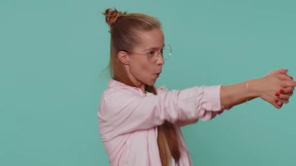 Pretty teenager girl pointing around with finger gun gesture, looking confident, making choice, shooting killing with hand pistol right on target. Young child kid isolated on blue studio background - Felvétel, videó