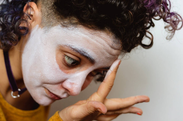 close-up of young latin caucasian woman, applying white paint on her face with her finger, to put on "la calavera catrina" makeup to celebrate the day of the dead. - Valokuva, kuva