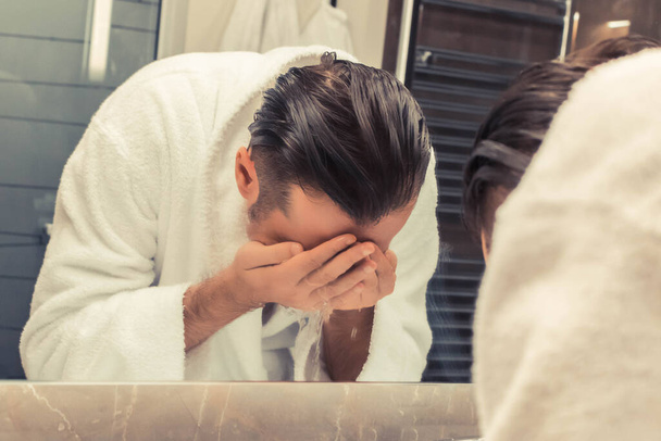 Віддзеркалення у дзеркалі людини в халаті, що миє обличчя вранці
. - Фото, зображення