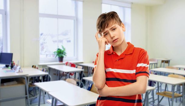 education, school and people concept - portrait of sad thinking boy in red polo t-shirt over classroom background - Фото, зображення