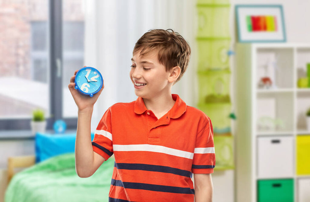 time management and people concept - portrait of happy smiling boy in red polo t-shirt with alarm clock over home room background - Foto, immagini