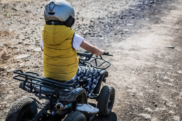 Back view of kid learning to drive four wheeled quad bike on dirt road. - Fotó, kép