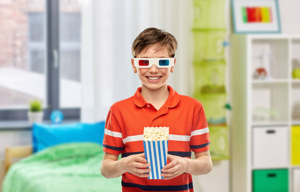 cinema, leisure and people concept - portrait of happy smiling boy in 3d movie glasses eating popcorn from striped bucket over home room background - Photo, image