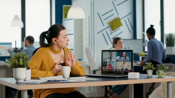Startup office employee using laptop in video conference with clients and manager talking about marketing strategy. Casual business woman in group call discussing with remote coworkers about charts. - Foto, imagen