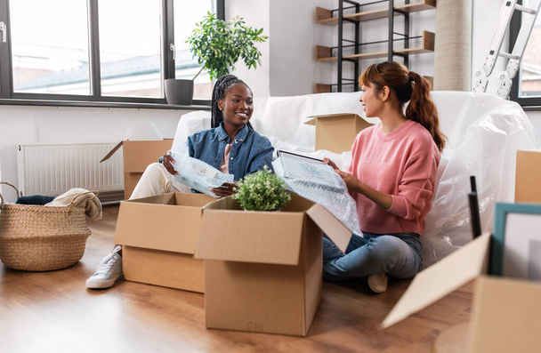 moving, people and real estate concept - happy smiling women packing or unpacking boxes at home - Foto, Bild