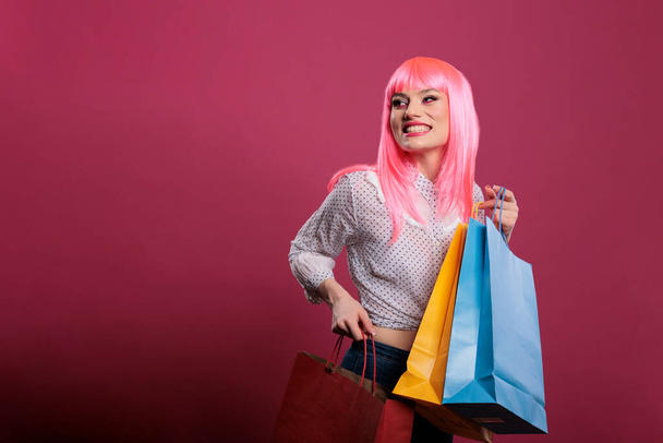 Female customer carrying retail store colorful shopping bags, using sale discount to purchase fashionable clothes. Holding packages after buying stylish things, modern fashion trend in studio. - Foto, imagen