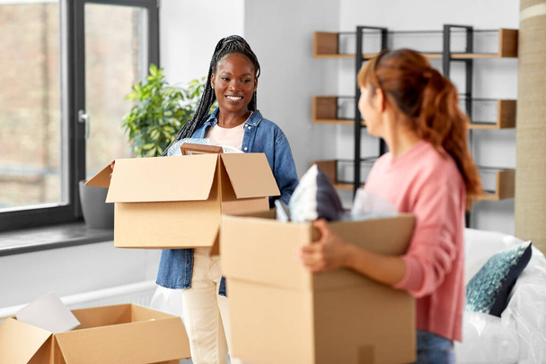 moving, people and real estate concept - happy smiling women with boxes at new home - Photo, Image