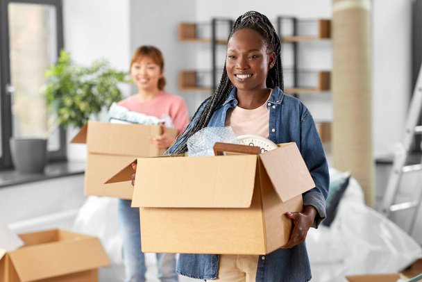 moving, people and real estate concept - happy smiling women with boxes at new home - Foto, Imagem