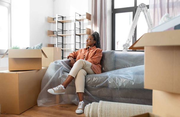 moving, people and real estate concept - happy smiling woman with boxes sitting on sofa at new home - Foto, Imagem