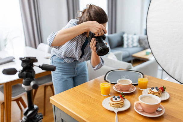 blogging, profession and people concept - female food photographer with camera photographing pancakes, coffee and orange juice in kitchen at home - Photo, image