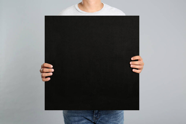Man holding black blank poster on grey background, closeup. Mockup for design - Fotó, kép