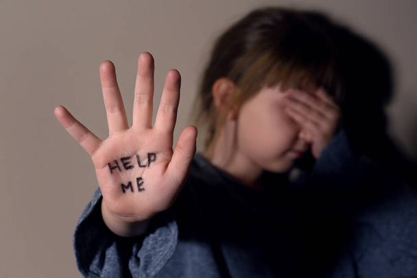 Плачущая маленькая девочка показывает ладонь с фразой "Помоги мне возле бежевой стены", сосредоточься на руке. Концепция домашнего насилия
 - Фото, изображение