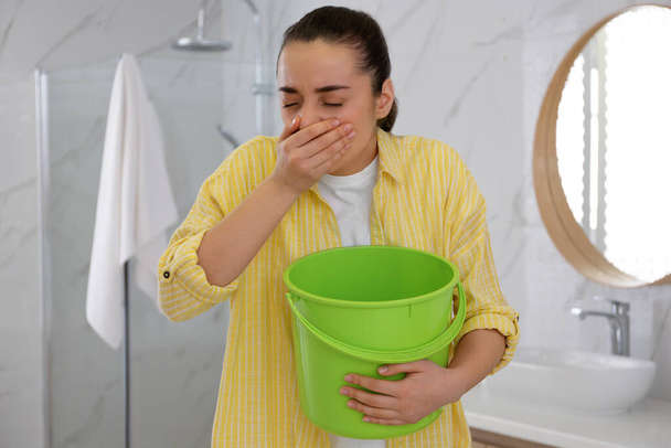 Young woman with bucket suffering from nausea in bathroom. Food poisoning - Photo, image