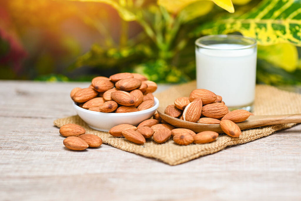 Almond milk and Almonds nuts on white bowl with green leaf on sack background, Delicious sweet almonds on the wooden table , roasted almond nut for healthy food and snack - Fotó, kép
