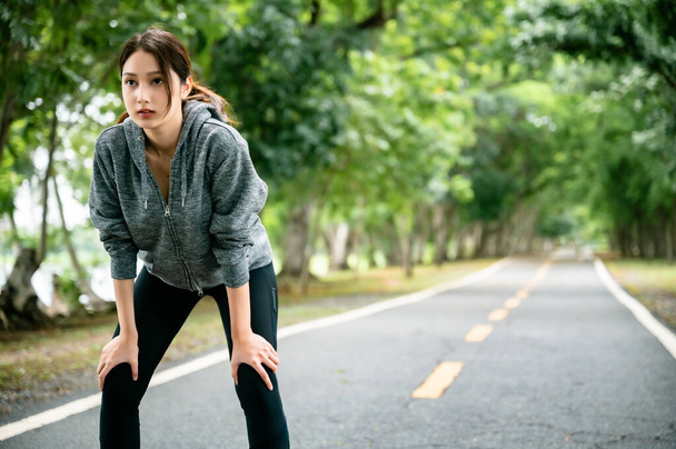 Aziatische vrouw draagt jas en is moe van fitness in het openbaar park. Haar blik was vastbesloten om gewicht te verliezen. Gezond leefstijlconcept - Foto, afbeelding