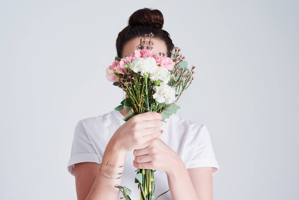 Квіти відображають те, хто ми є. Студійний знімок невпізнаваної жінки, що прикриває обличчя квітами на сірому фоні
 - Фото, зображення