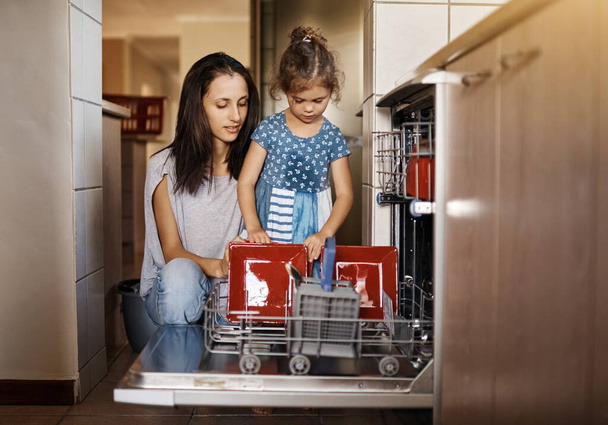 Raising one responsible little girl. a cute little girl and her mother loading the dishwasher together at home - Foto, immagini