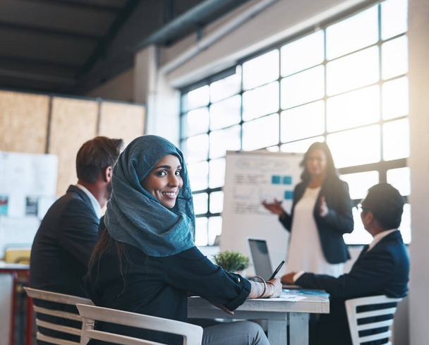 Making big moves in the boardroom. Portrait of a smiling arab businesswoman attending a presentation with her colleagues in the office - 写真・画像