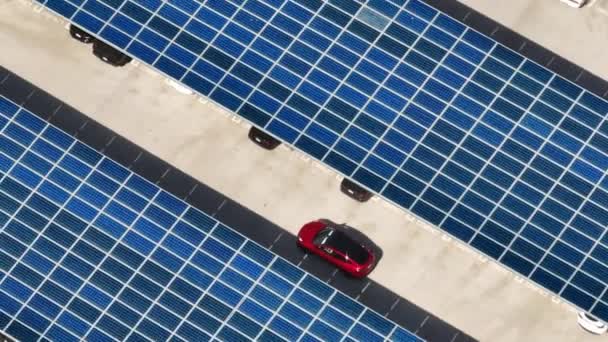 Cinematic urban transportation footage. Aerial view of red vehicle driving by rooftop parking lot with scenic blue solar batteries on outdoor parking lot with many cars parked at shopping mall USA 4K - Imágenes, Vídeo