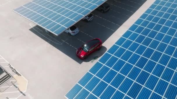 Aerial red electric car on rooftop parking with solar panels. Zero pollution car, green energy concept on modern rooftop parking lot. Alternative energy for ecological cars under blue solar batteries - Materiał filmowy, wideo