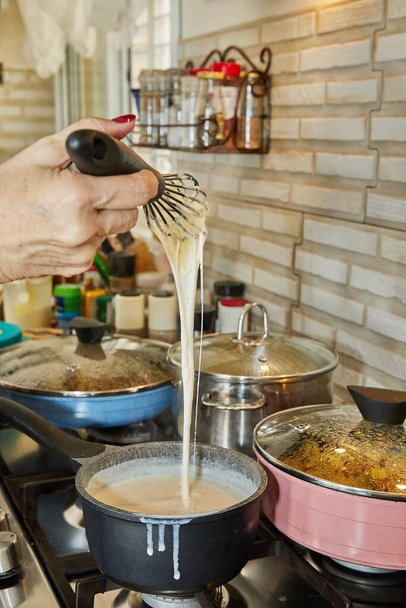 Chef stirs the bechamel sauce, which is cooked on gas stove, into saucepan. - Foto, Bild