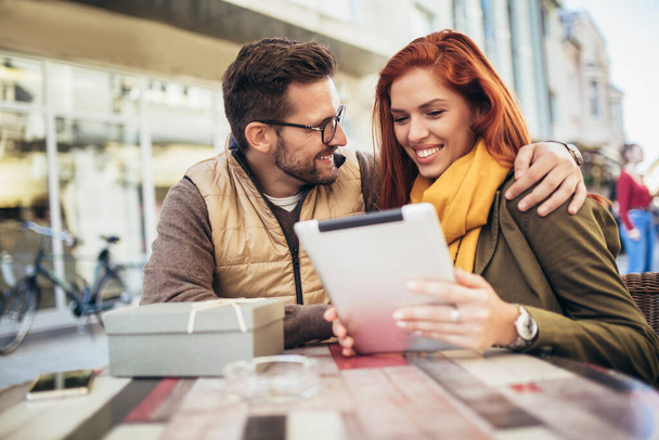 Счастливая молодая пара использует цифровой планшет вместе в кофейне. Молодой человек и женщина смотрят на сенсорный экран компьютера и улыбаются. - Фото, изображение