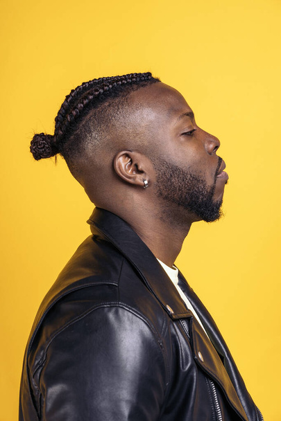 African american man with cool hairstyle and wearing black leather jacket posing in studio shot against yellow background. - Fotografie, Obrázek