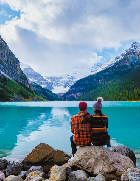Національний парк Луїза Банф - озеро в Канадських Скелястих горах. Молода пара чоловіків і жінок сидять на скелі біля озера під час холодного дня восени в Канаді. - Фото, зображення