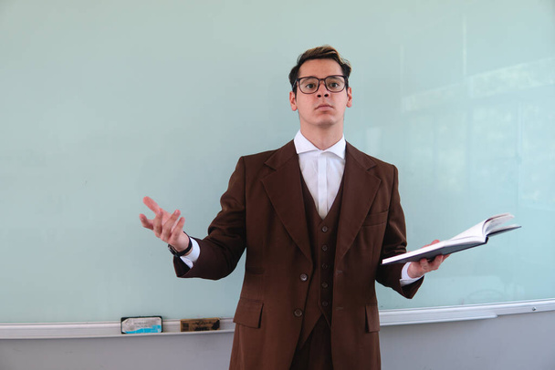 Blond Caucasian man in a suit and glasses giving a class and asking questions to his students. Teacher with questions about his class. Teacher in a classroom giving classes. High quality photo - Foto, immagini