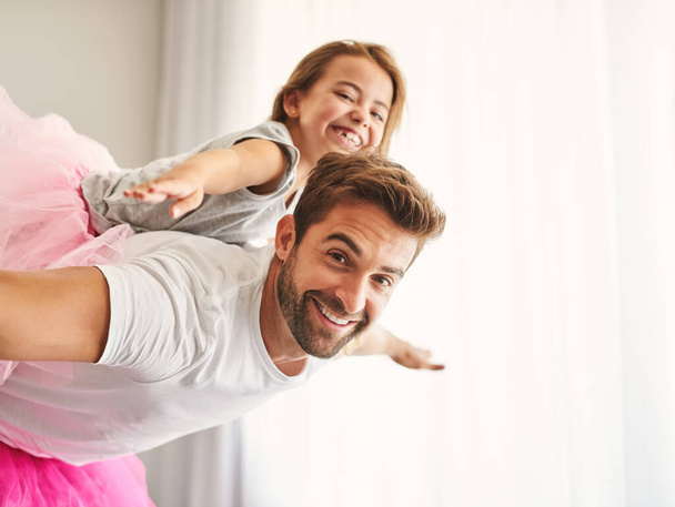 Ill teach her how to sore. Cropped portrait of a handsome young man piggybacking his daughter at home - 写真・画像
