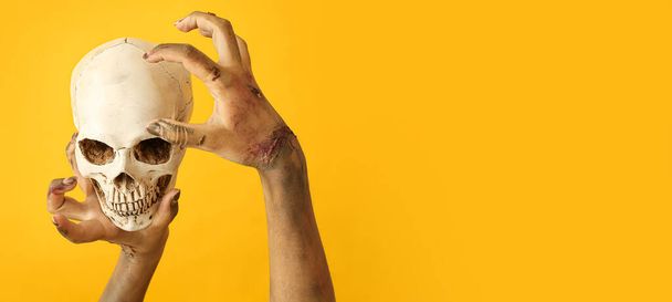 Hands of zombie with human skull on yellow background. Halloween concept - Valokuva, kuva