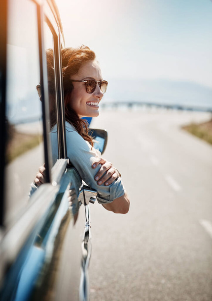 I love feel the breeze against my face. an attractive woman hanging out of a car window while enjoying a road trip - Valokuva, kuva