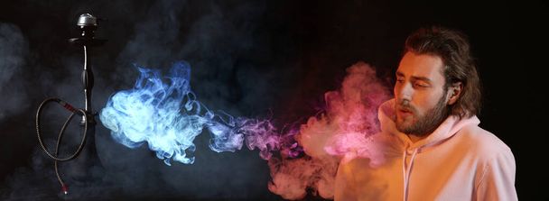 junger Mann raucht Wasserpfeife auf dunklem Hintergrund   - Foto, Bild