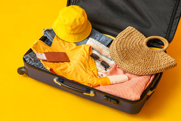 Βαλίτσα με ρούχα, αξεσουάρ παραλίας, εισιτήριο και διαβατήριο σε κίτρινο φόντο - Φωτογραφία, εικόνα